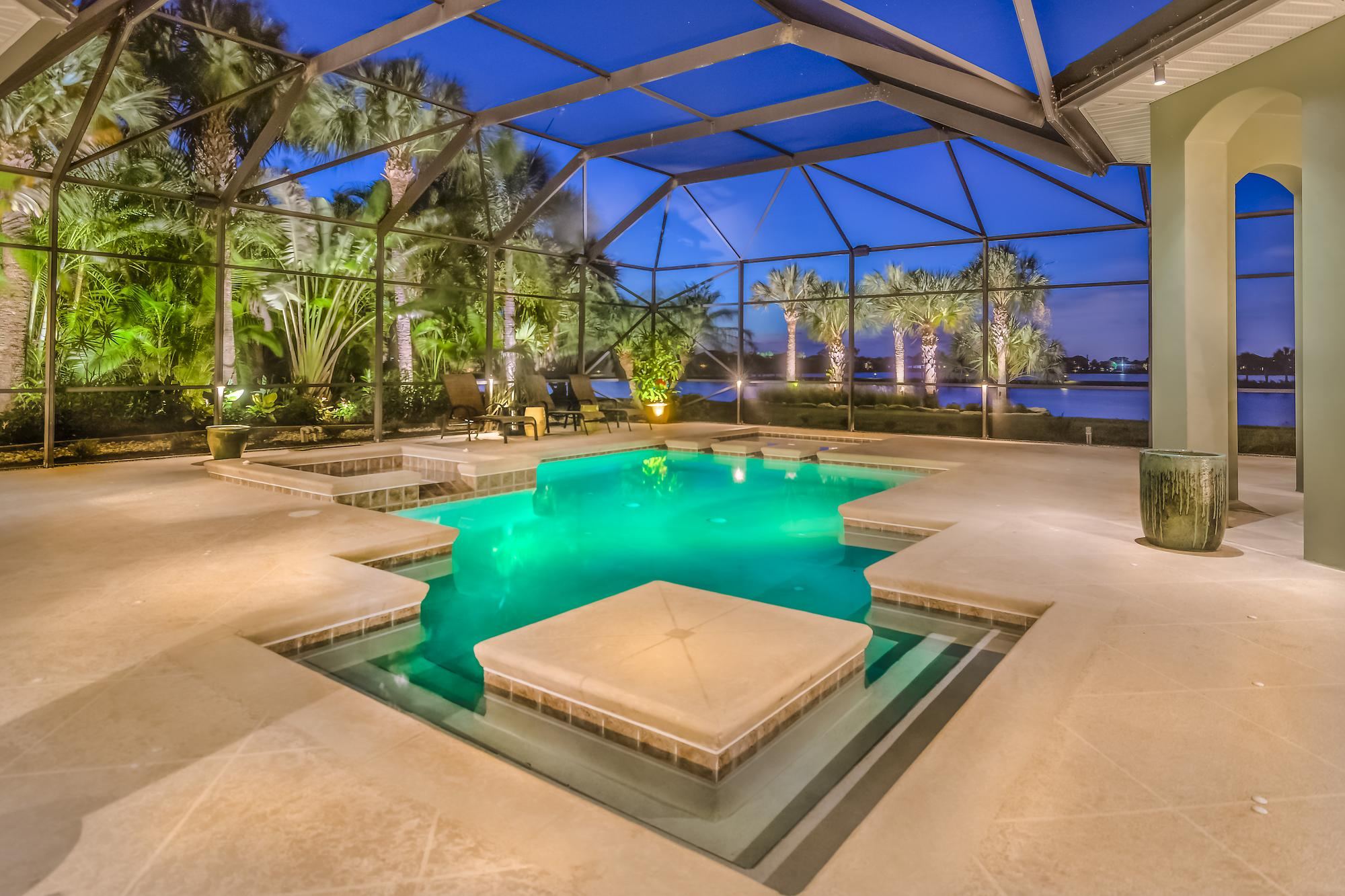A finished South Florida pool glowing turquoise at dusk inside a screened enclosure