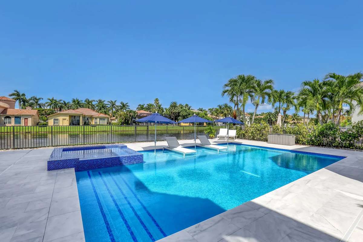 A newly finished South Florida backyard pool with bright turquoise water, a raised spa and palm trees