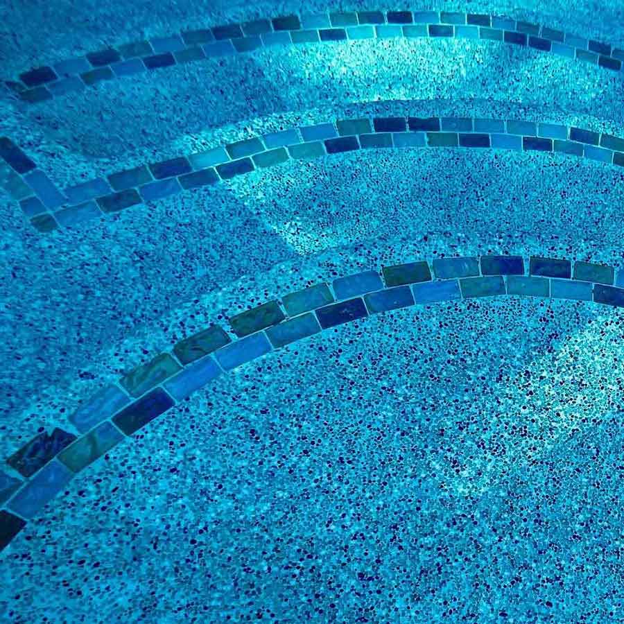Blue glass tile step markers set into a sparkling aggregate pool finish, seen through clear water
