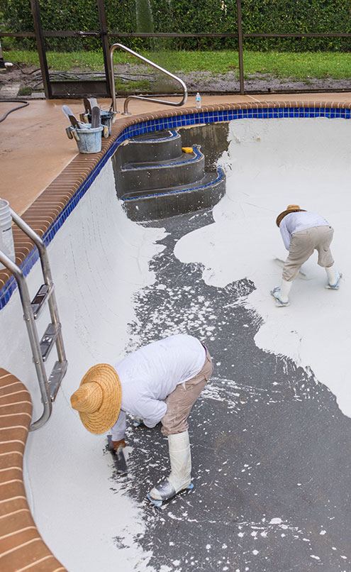 Chief Pools crew members applying a fresh finish inside a drained backyard pool